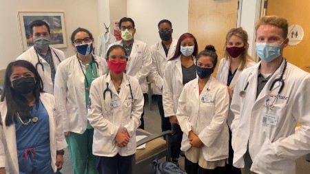 students in white coats wearing surgical masks in a clinical setting